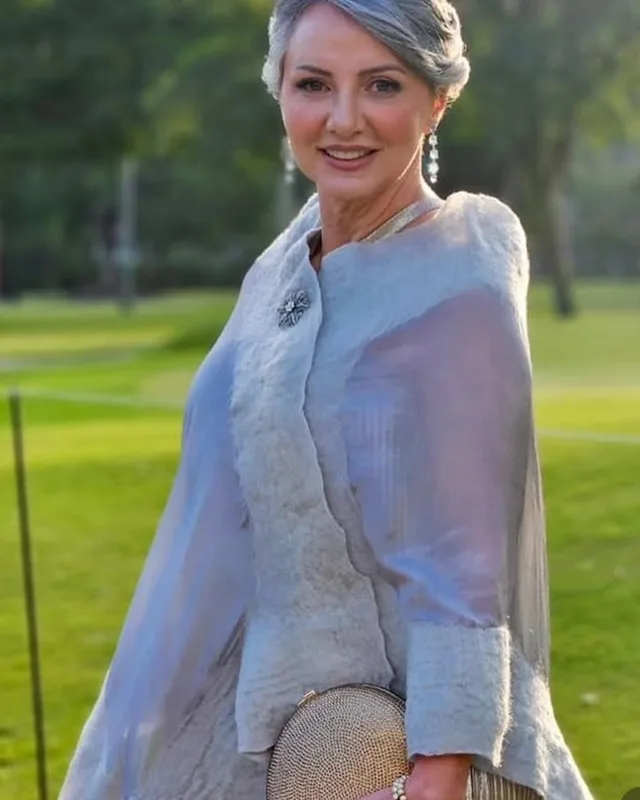 Senhora de cabelo grisalho, vestido azul-acinzentado, num jardim